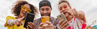 Tres amigos se divierten mirando sus móviles, haciendo como que hacen una foto al espectador